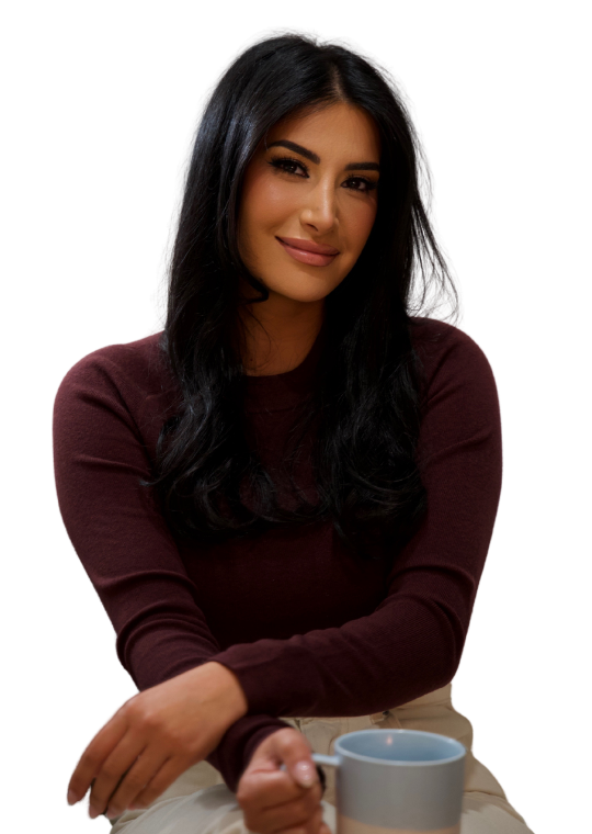 A woman with long dark hair, wearing a maroon long-sleeve top, sits and smiles while holding a gray mug. The background is white.